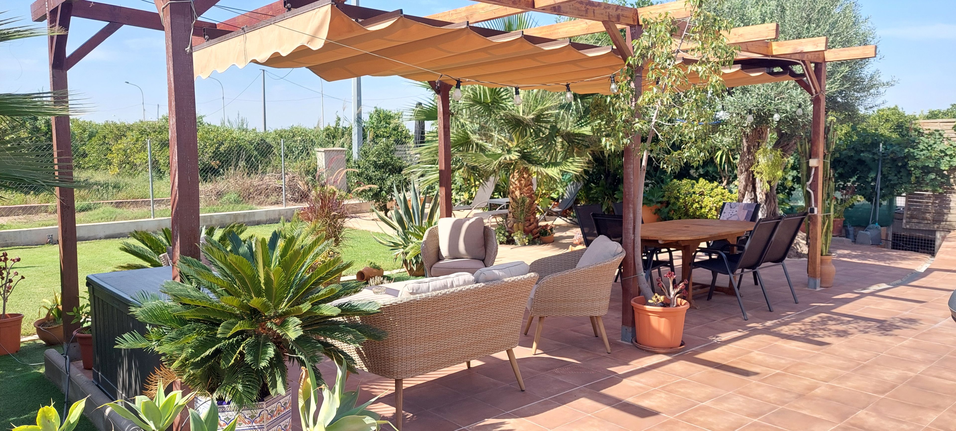 An outdoor patio with a pergola, wicker furniture, a table, and chairs.