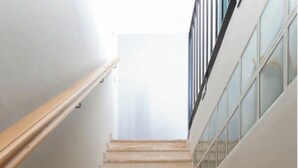 Een trap met houten leuning en glazen balustrades, die leidt naar een verdieping.