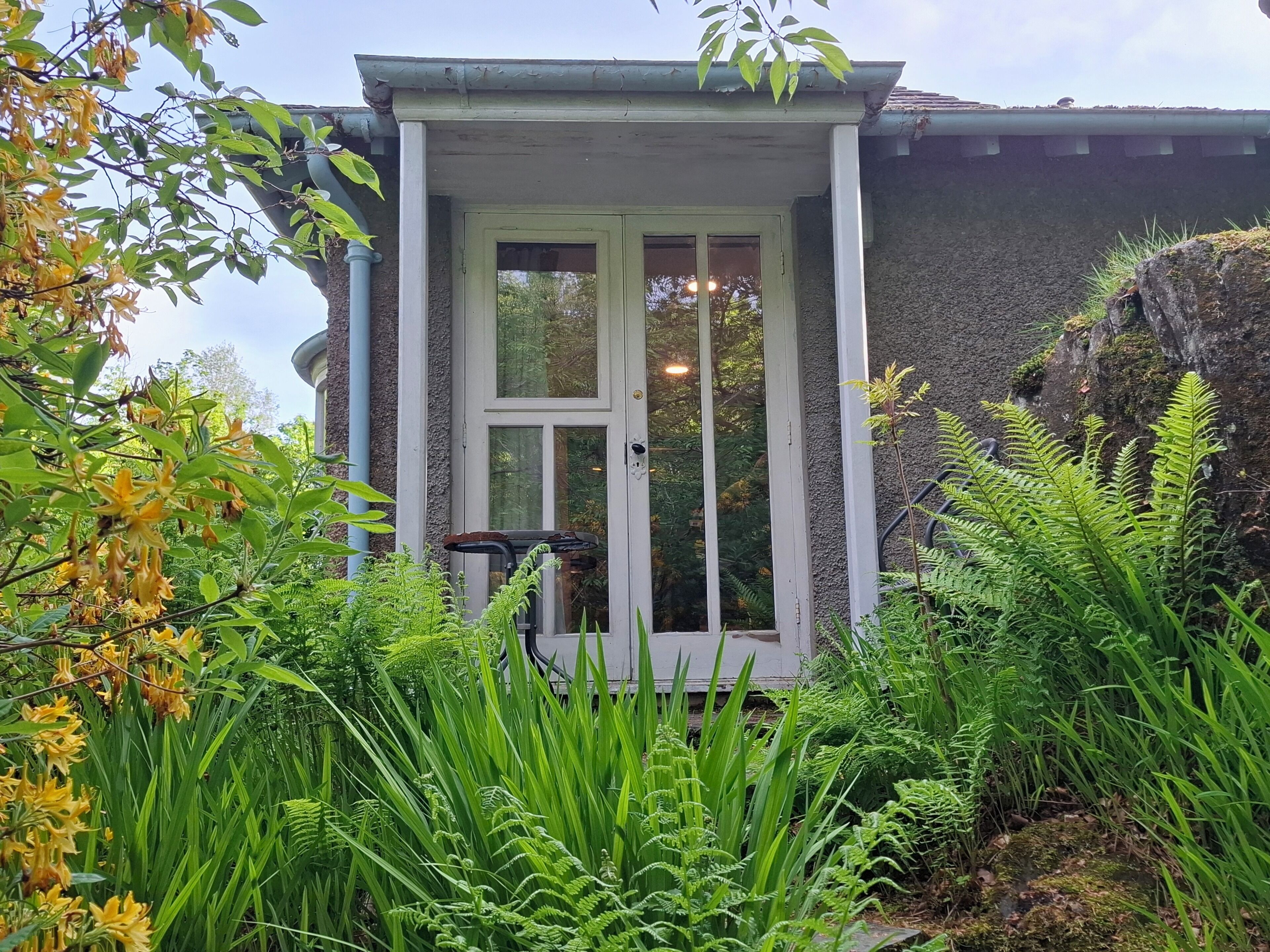 A house with a white door, a small porch, and lush greenery.
