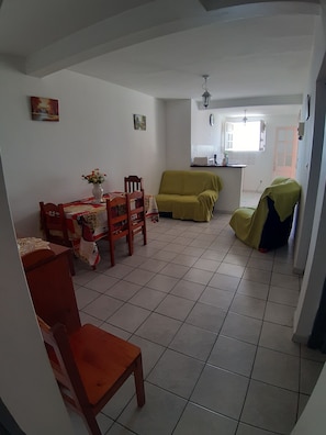 A living room with a dining table, chairs, a sofa, and a kitchen area in the background. - The waterfront (Les Anses-d'Arlet)