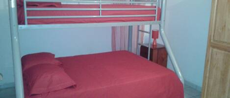 A bunk bed with red bedding in a room with a wooden cabinet and a window with curtains.