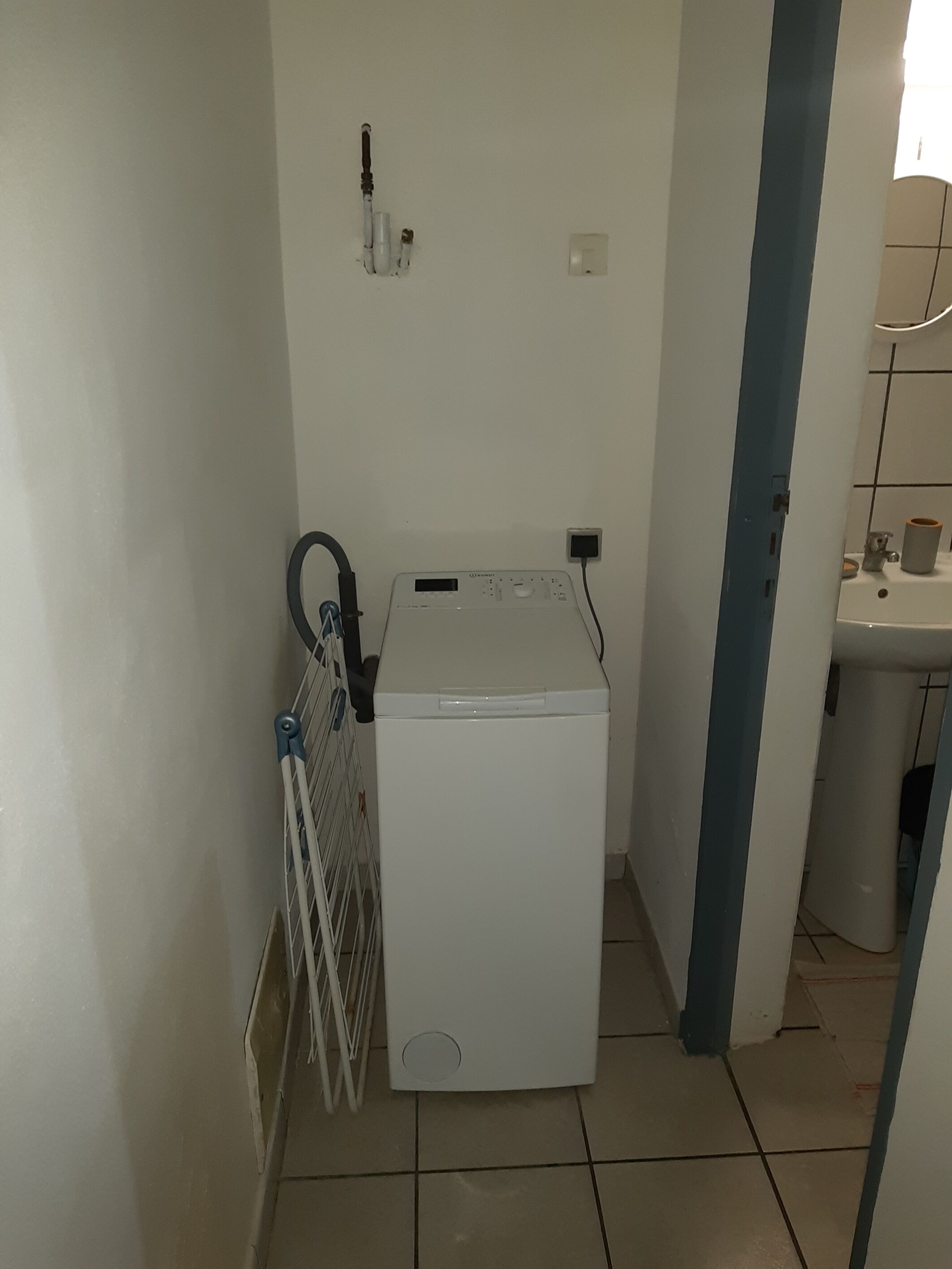 A compact laundry room with a front-loading washing machine, a drying rack, and a sink.