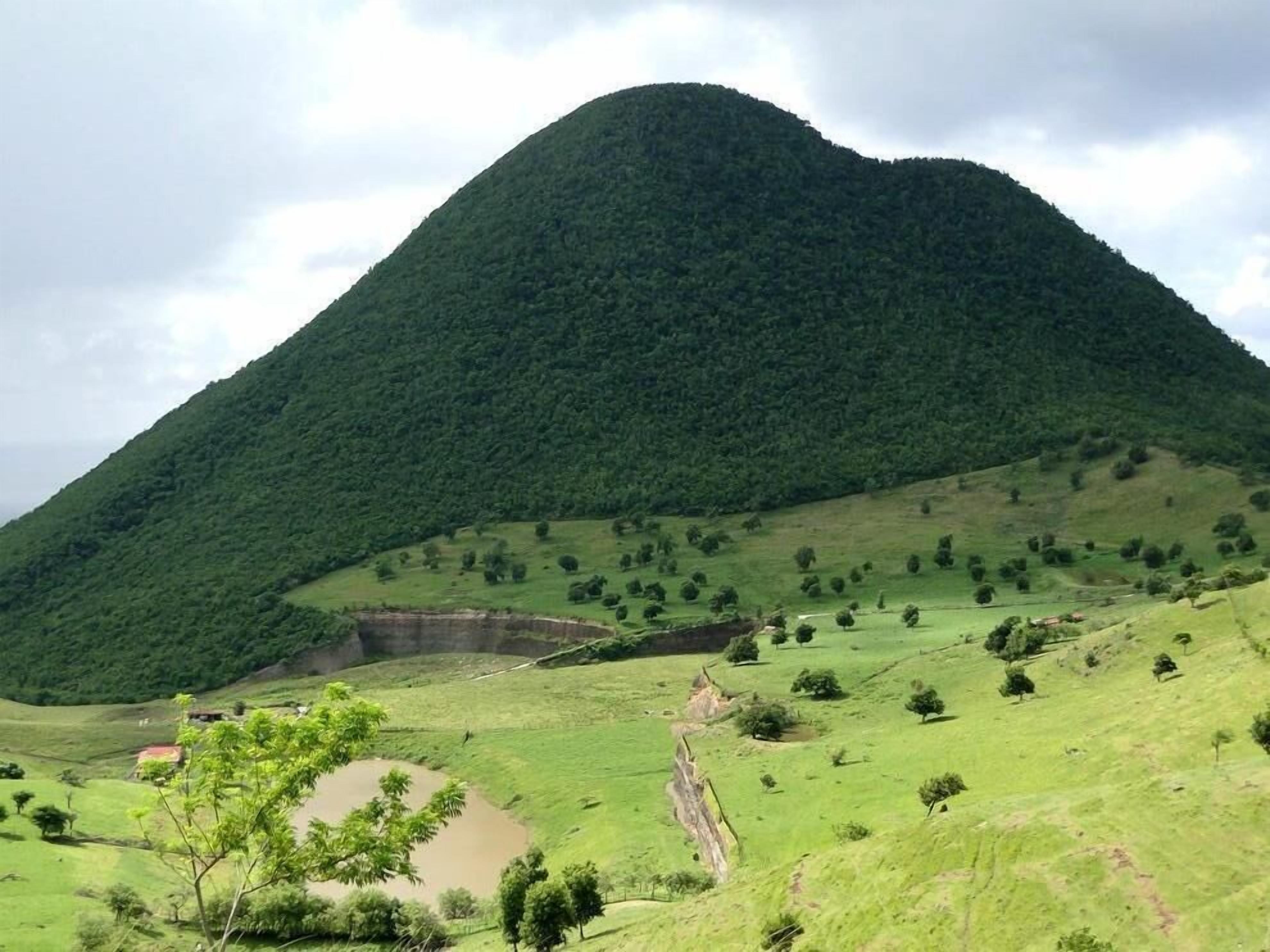 Eine gebirgige Landschaft mit einem Tal, vereinzelten Bäumen und einem kleinen Gewässer.