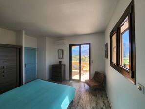 Relax in this serene bedroom with a large bed, dresser, and chair, offering a balcony with a view of the surrounding landscape.