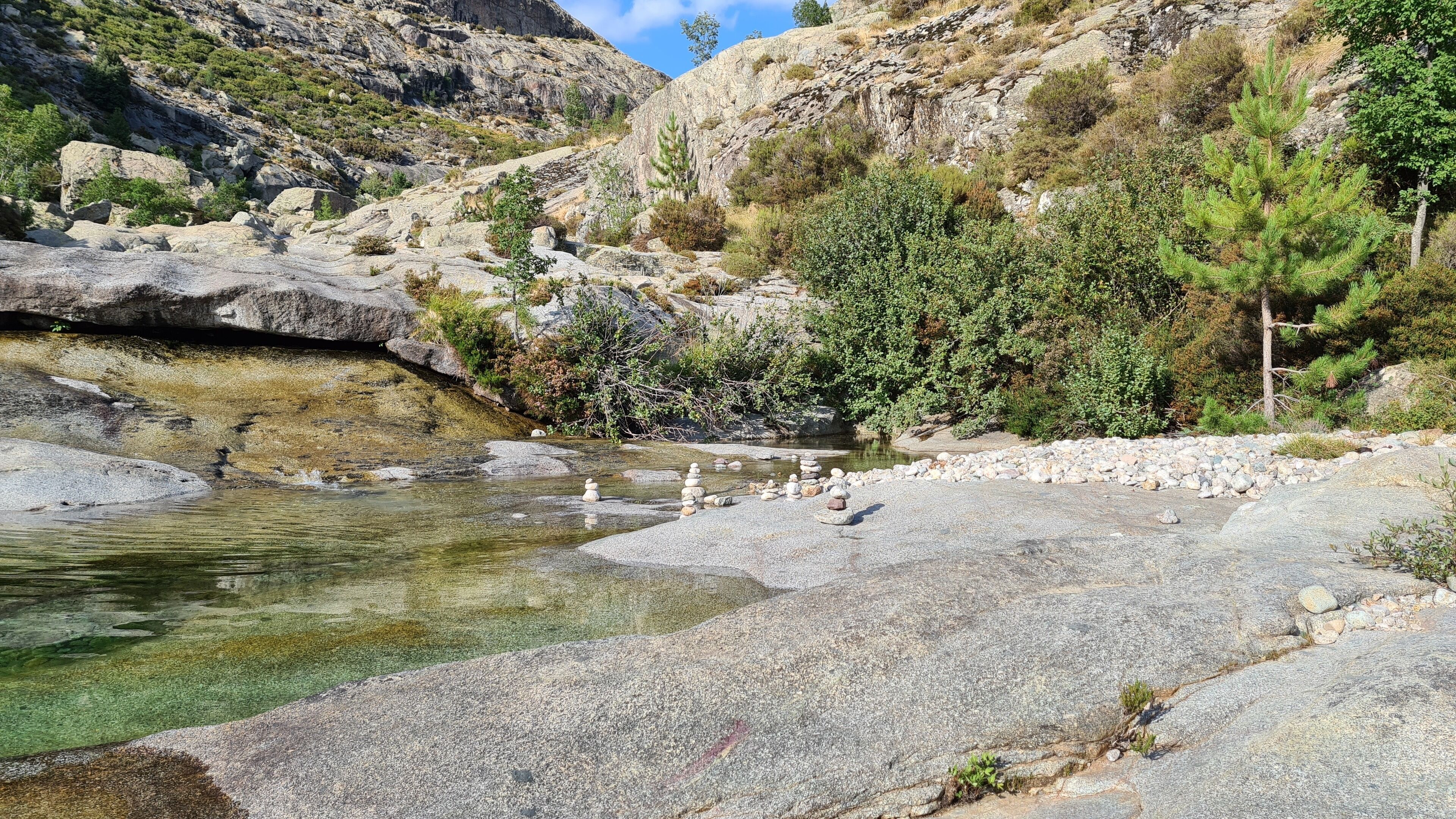 A rocky landscape with a clear stream and sparse vegetation.
