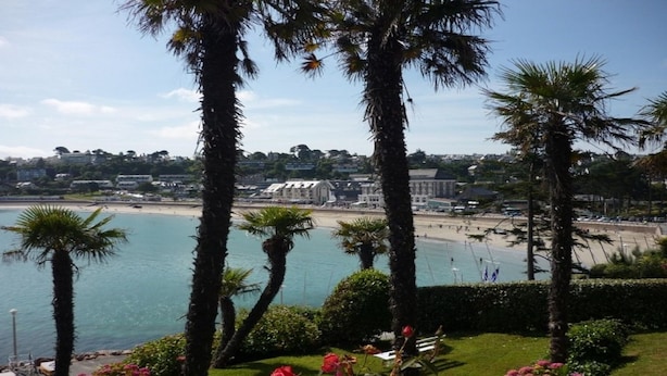 A coastal view with palm trees, a beach, and buildings in the background.