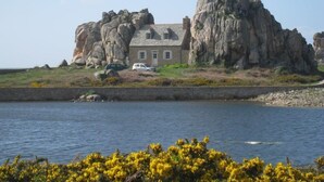 A house on a rocky cliff by the sea with a car parked in front.