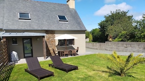 A house with a patio, two lounge chairs, a table, and a covered outdoor area.