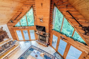 A log cabin interior with a fireplace, wooden benches, and a large window with a deer head decoration. - Beautiful Log Cabin Near Devil’s Lake (baraboo)