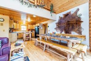 Een rustiek interieur met houten vloeren, een grote houten eettafel en een opvallend kunstwerk aan de muur.