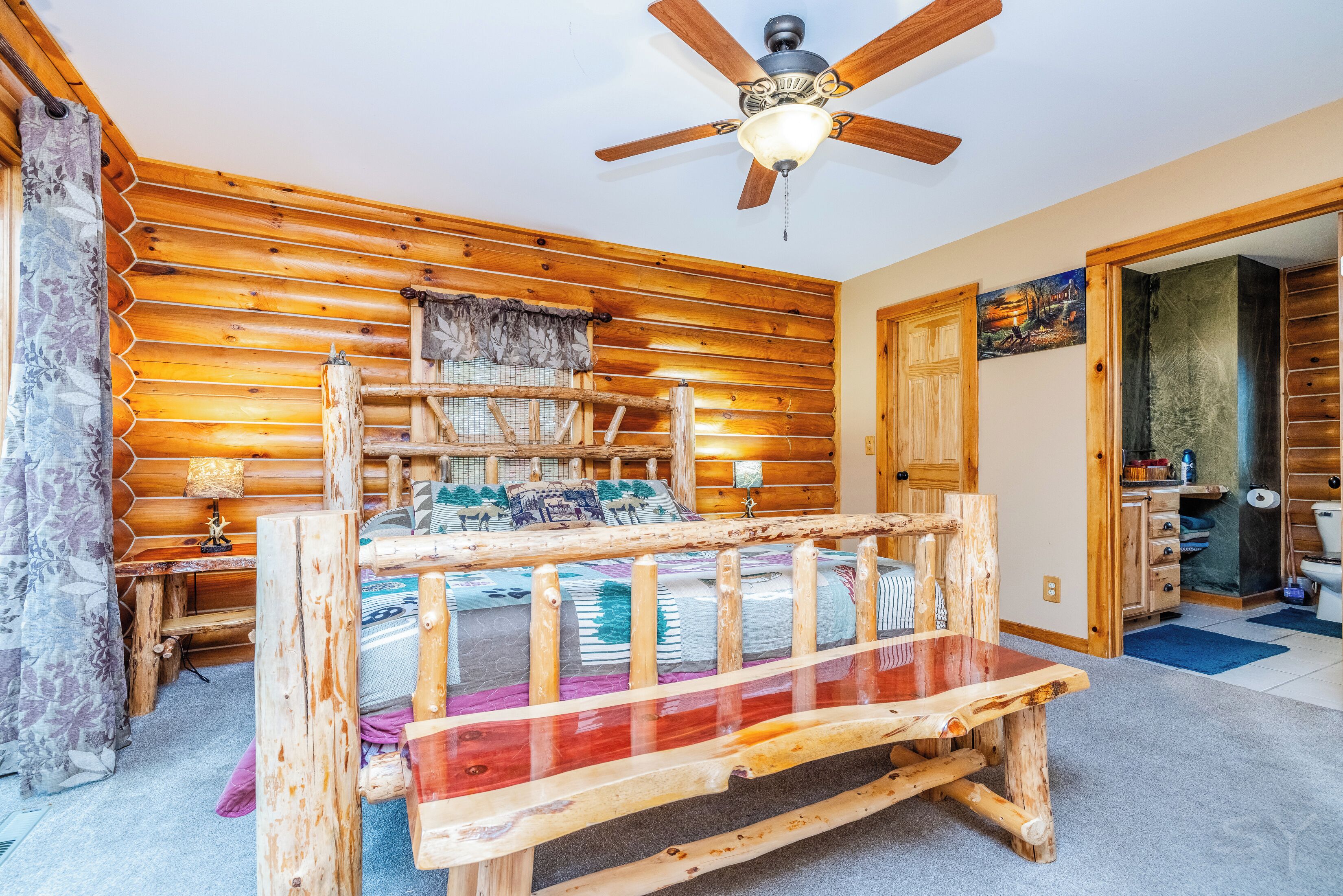 Una habitación tipo cabaña de madera con una cama de madera, un ventilador de techo y una puerta que da a un baño.