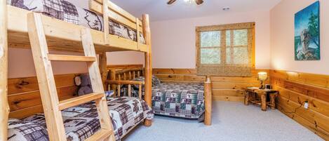 A bunk bed room with a ceiling fan, a window with bamboo blinds, and a small table with a lamp.
