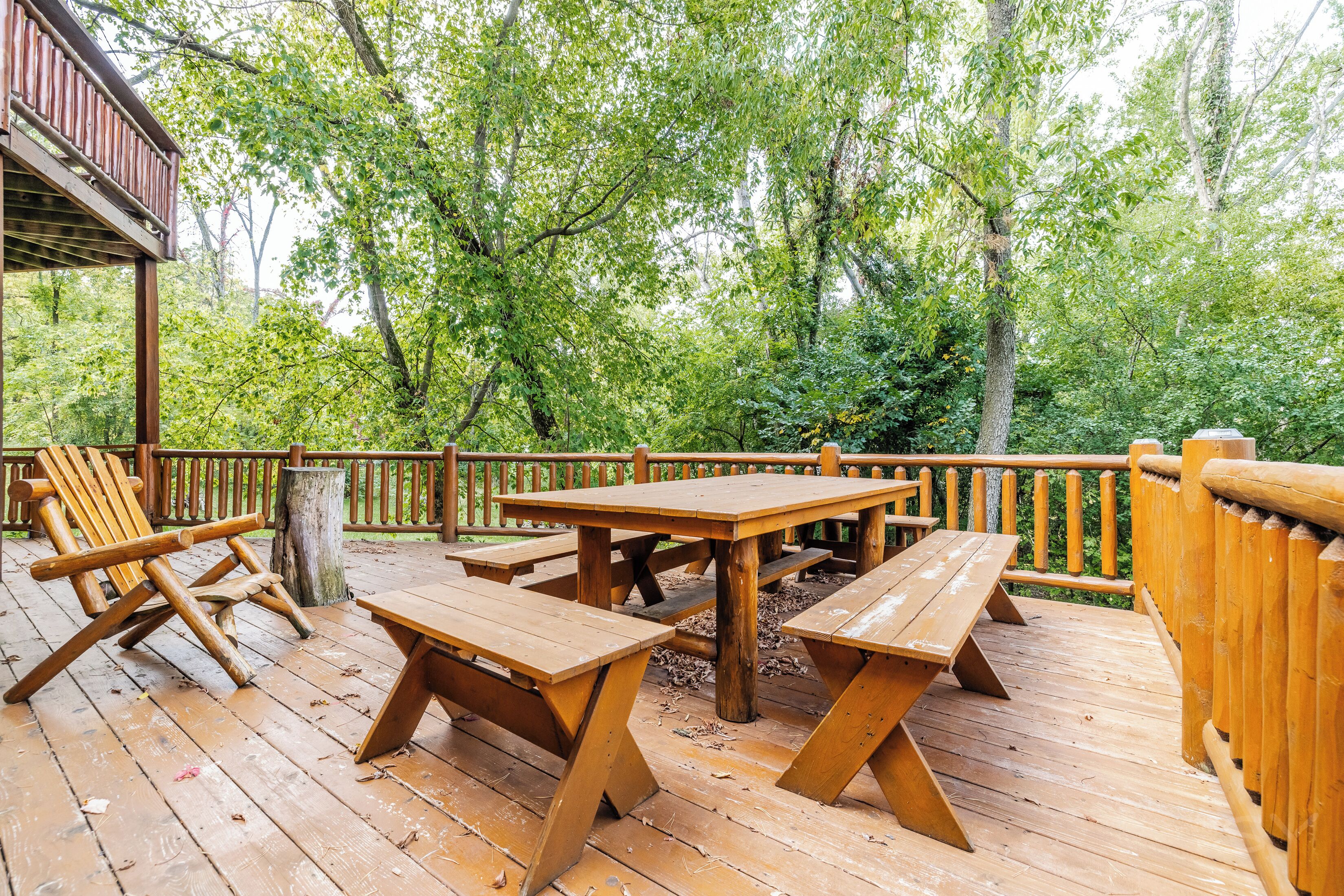 Eine Holzterrasse mit Picknicktischen und -stühlen, umgeben von Bäumen.