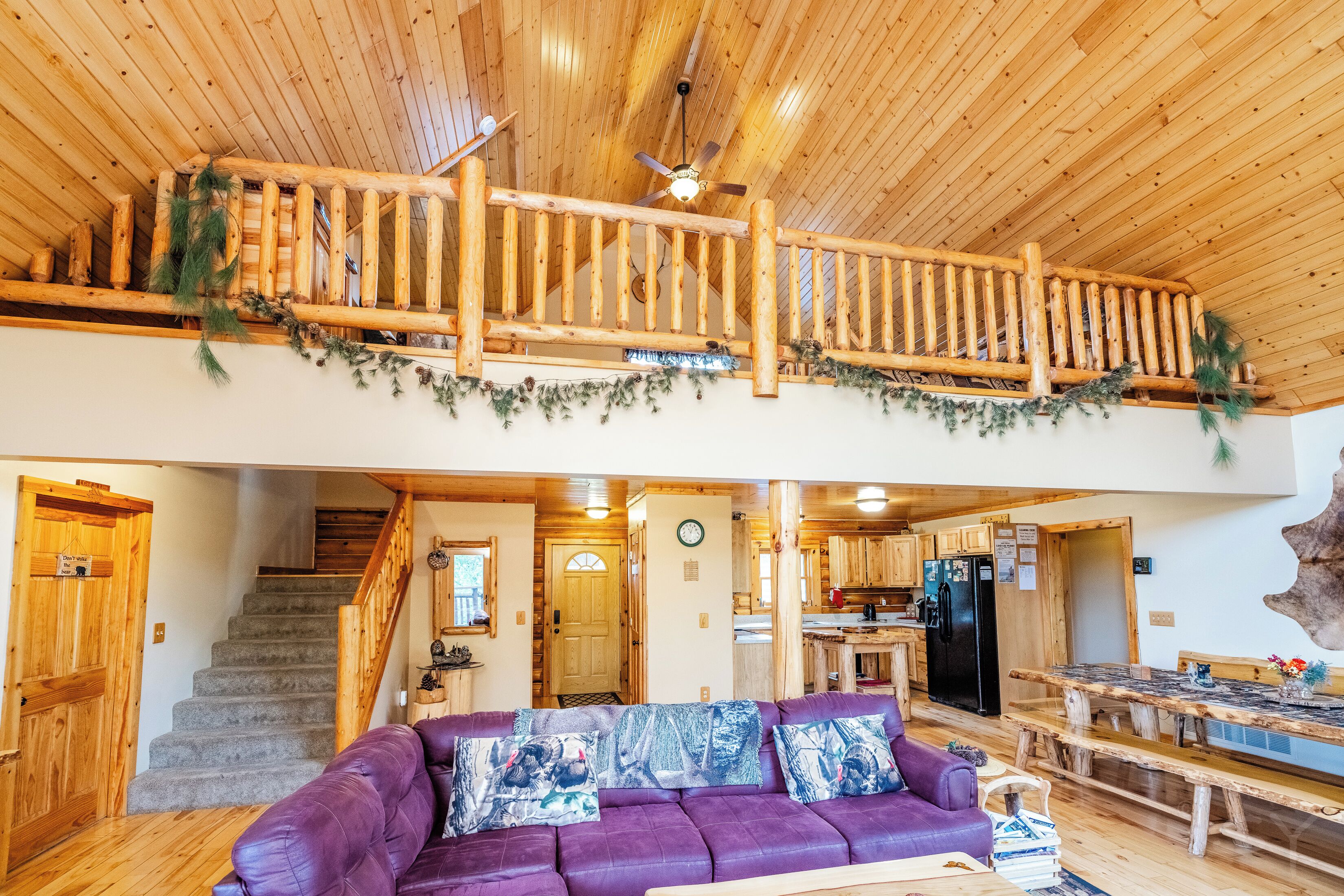 A wooden interior with a purple sofa, a staircase, a kitchen, and a dining area.