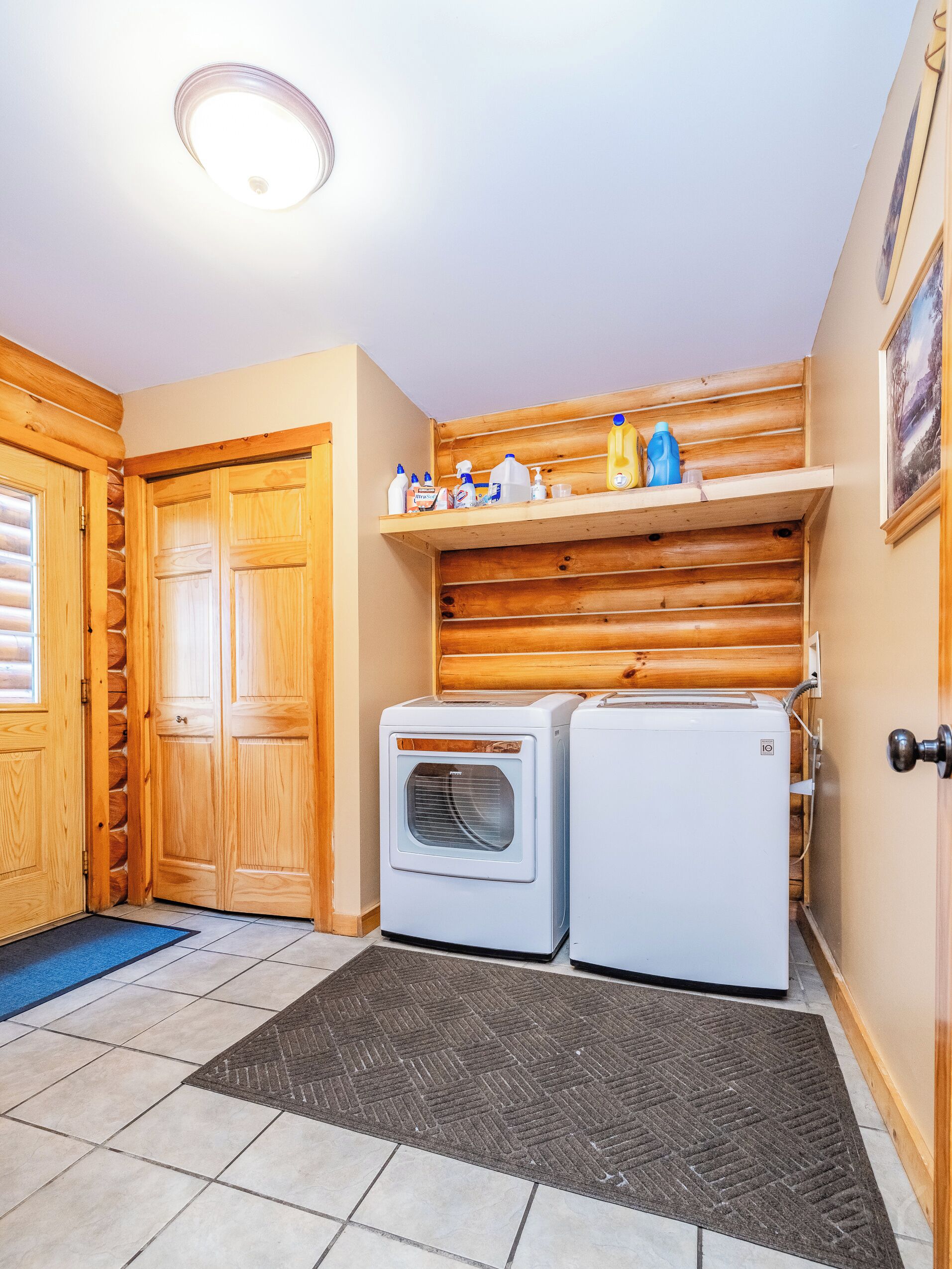 Un cuarto de lavandería con puertas de madera, una lavadora, un secador y un estante con artículos de limpieza.