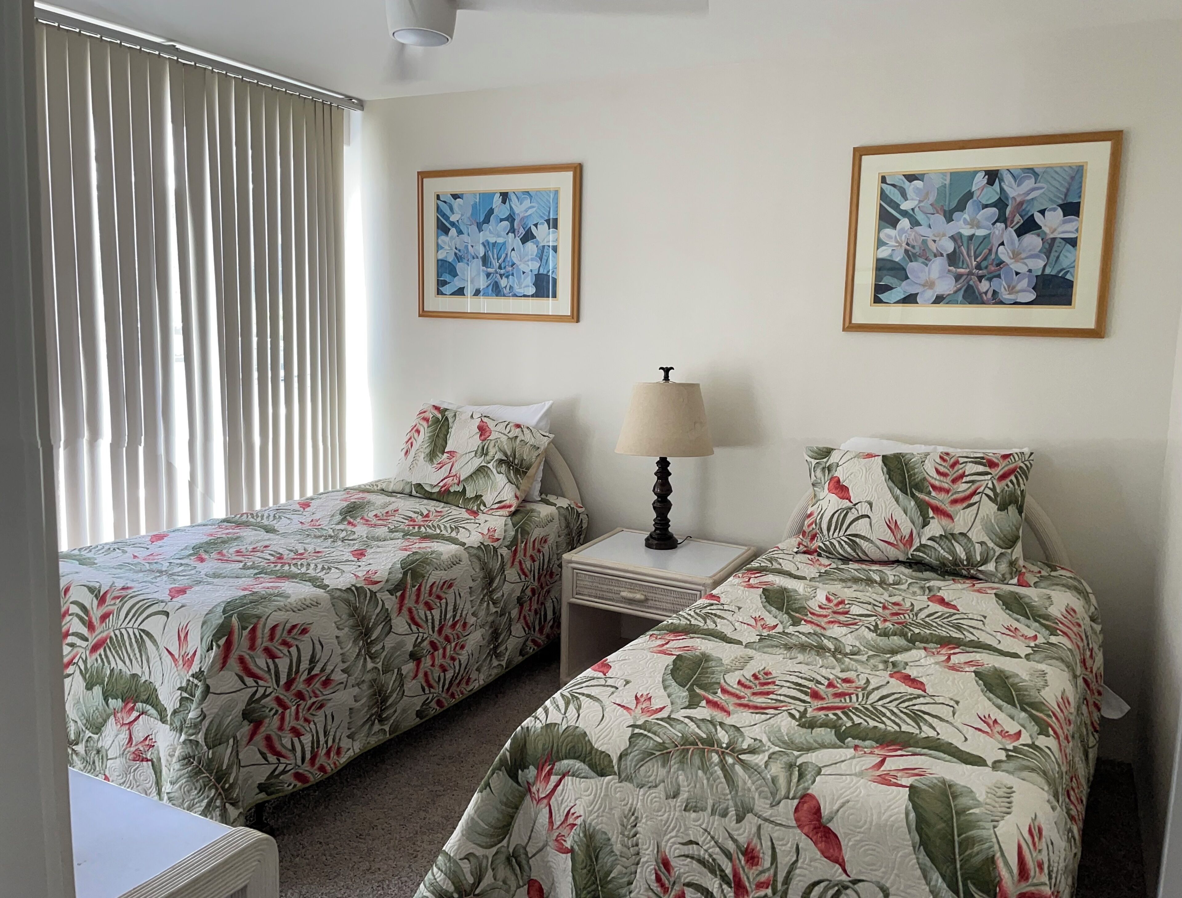 Een hotelkamer met twee bedden, elk met bloemenbeddengoed, een nachtkastje met een lamp, en twee florale schilderijen in lijsten aan de muur.