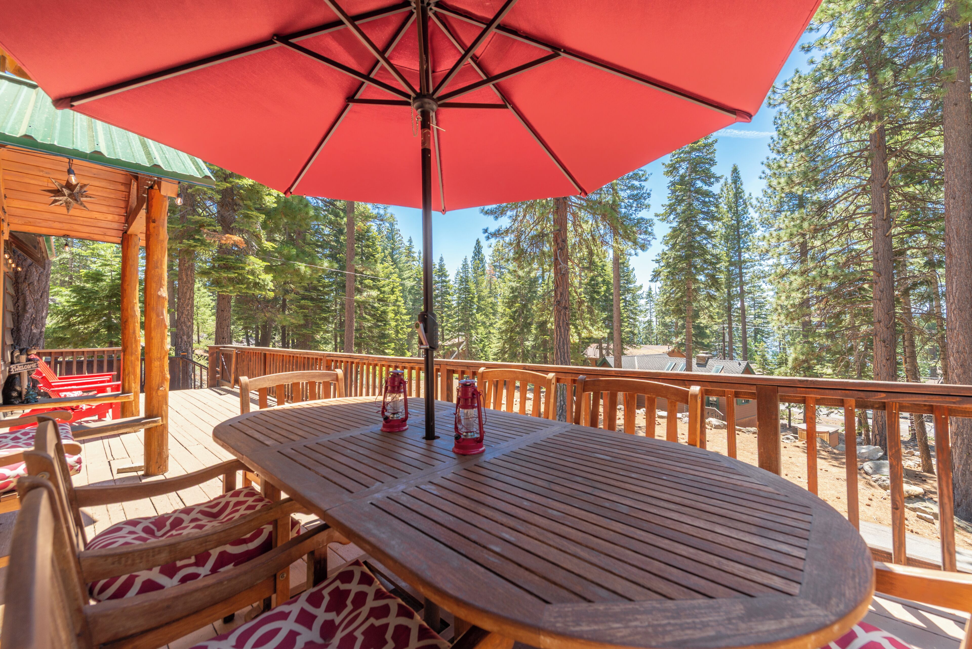 A wooden deck with a red umbrella, wooden chairs, and a table.
