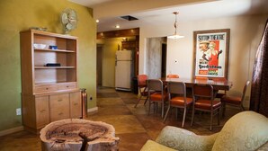 Uma sala de jantar com mesa e cadeiras de madeira, um ventilador e um cartaz na parede.