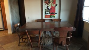 Uma área de jantar com mesa e cadeiras de madeira, um cartaz na parede e uma janela com cortinas.