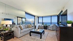Ein modernes Wohnzimmer mit großem Fenster und Meerblick, einer Couch, einem Couchtisch und einem Fernseher auf einem Schrank.