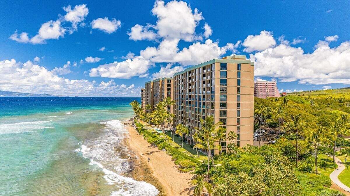 A beachfront hotel with a clear view of the ocean, a well-maintained lawn, and a parking area.