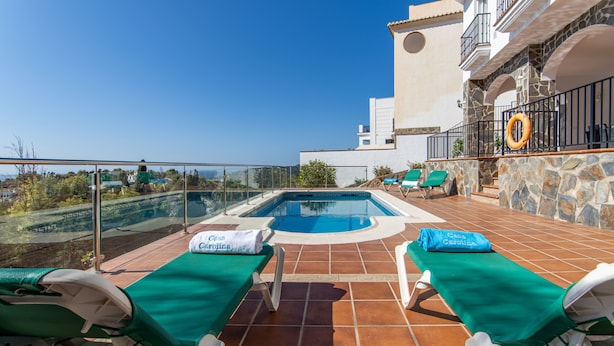 A rooftop pool area with two lounge chairs, a small pool, and a stone wall.