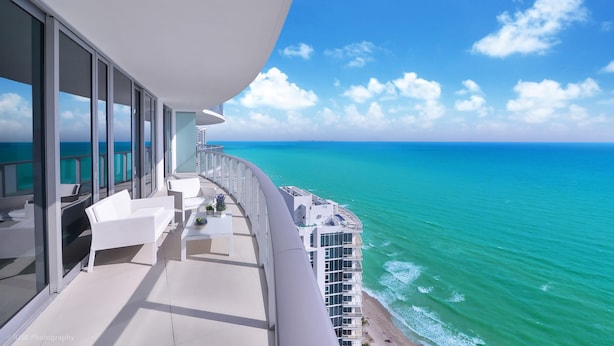 Un balcon avec vue sur l’océan, des meubles blancs et une rambarde en verre.
