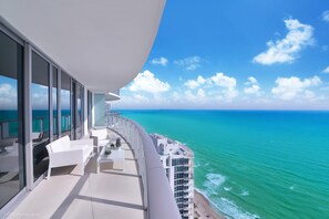 A balcony with a view of the ocean, white furniture, and a glass railing.