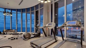 Une salle de sport moderne équipée de tapis de course, de vélos elliptiques et d’appareils de musculation, de grandes fenêtres offrant une vue sur la ville et d’un plafond aux lignes courbes.