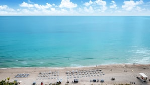 Ein Strand mit Liegestühlen, Sonnenschirmen, einem Rettungsturm und freiem Blick auf das Meer.