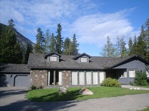 Stunning two-story house with a front entrance and porch area, set amidst a well-maintained lawn and surrounded by tall trees and a mountain.
