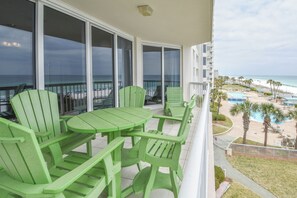 A balcony with green chairs and a table, overlooking a beach and a pool area.