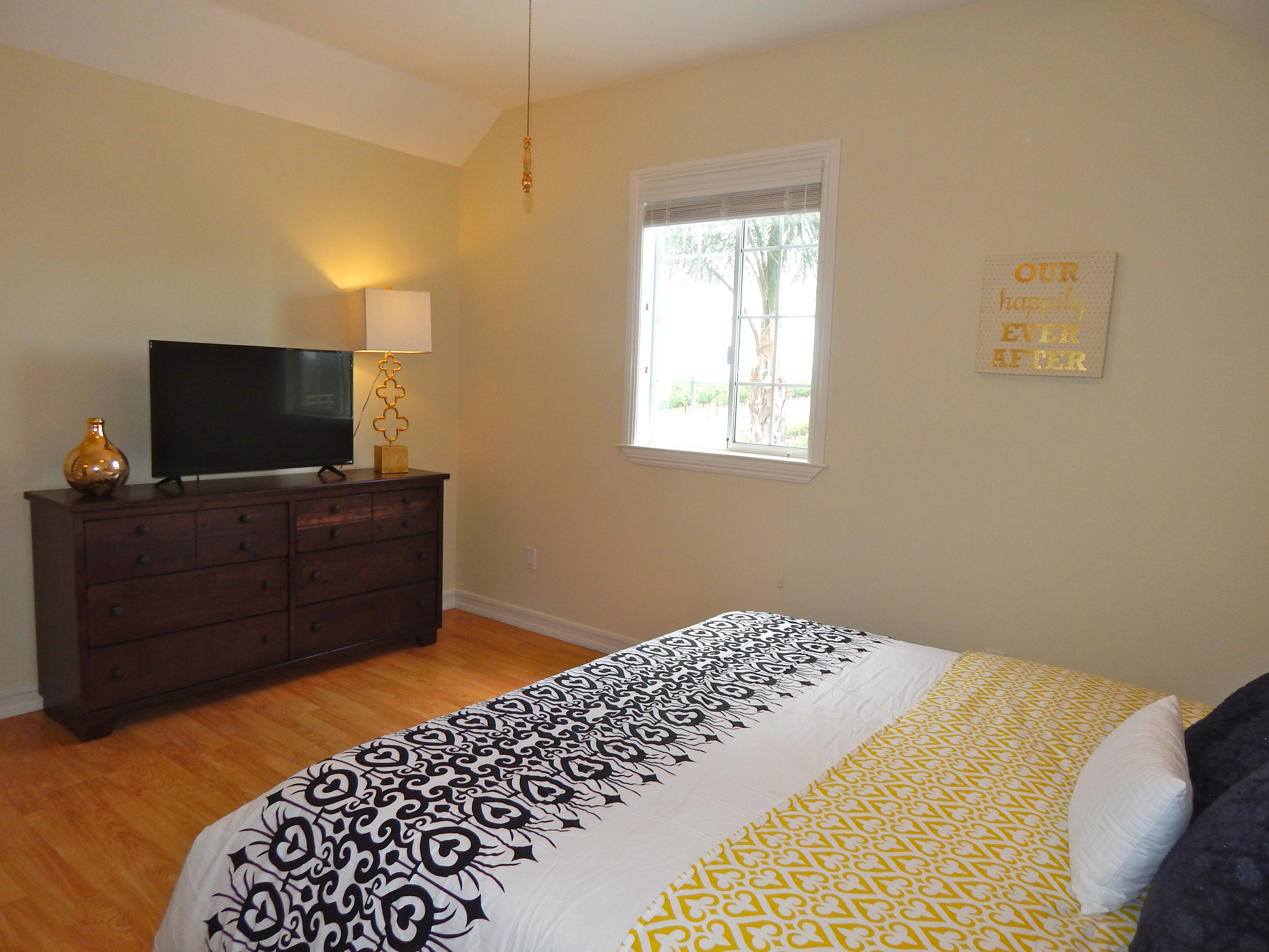 A bedroom with a bed, a dresser, a television, and a window.