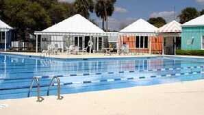 Una piscina amb gandules i ombrelles, envoltada de petites cabanes de platja.