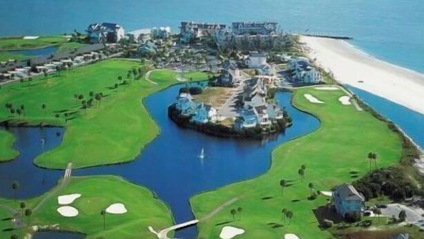Un complex turístic a la costa amb un camp de golf, elements aquàtics i propietats a peu de platja.