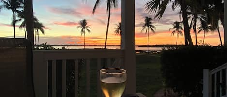 A table with a glass of white wine, overlooking a sunset with palm trees.