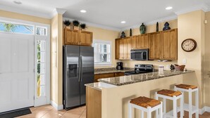 Una cocina moderna con un refrigerador de acero inoxidable, armarios de madera, un microondas y una isla grande con taburetes de bar.