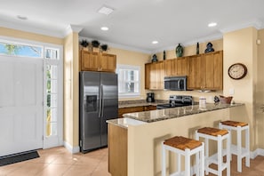 A modern kitchen with a stainless steel refrigerator, wooden cabinets, a microwave, and a large island with bar stools.