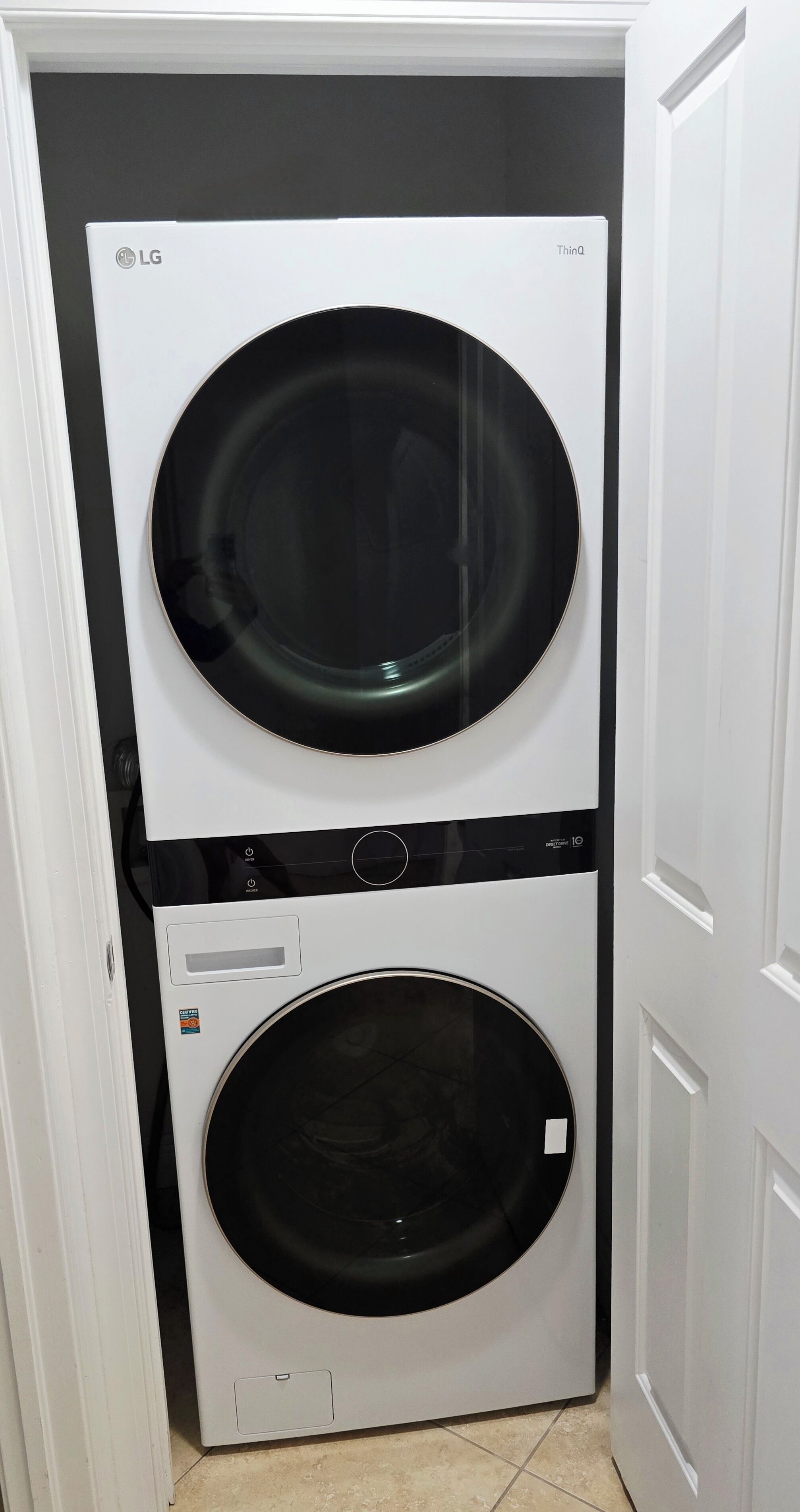 A white LG ThinQ washer and dryer unit in a corner of a room with white walls and a tiled floor.