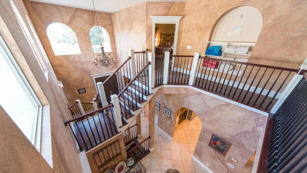 Ein mehrgeschossiges Interieur mit einer zentralen Treppe, Bogenfenstern und Blick auf ein Schlafzimmer.