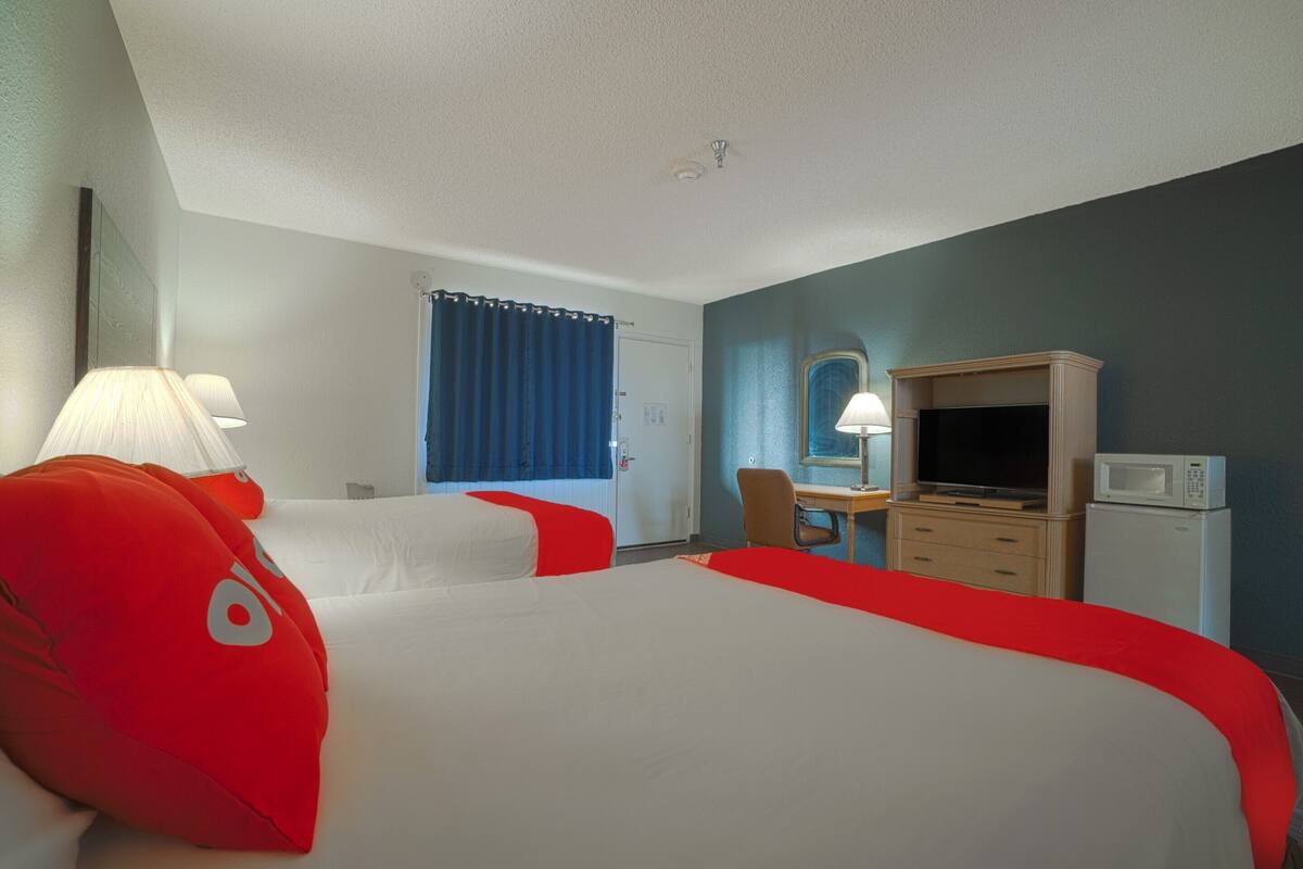 Ein Hotelzimmer mit zwei Betten, einem Schreibtisch, einem Fernseher, einer Mikrowelle und einem Fenster mit Vorhängen.