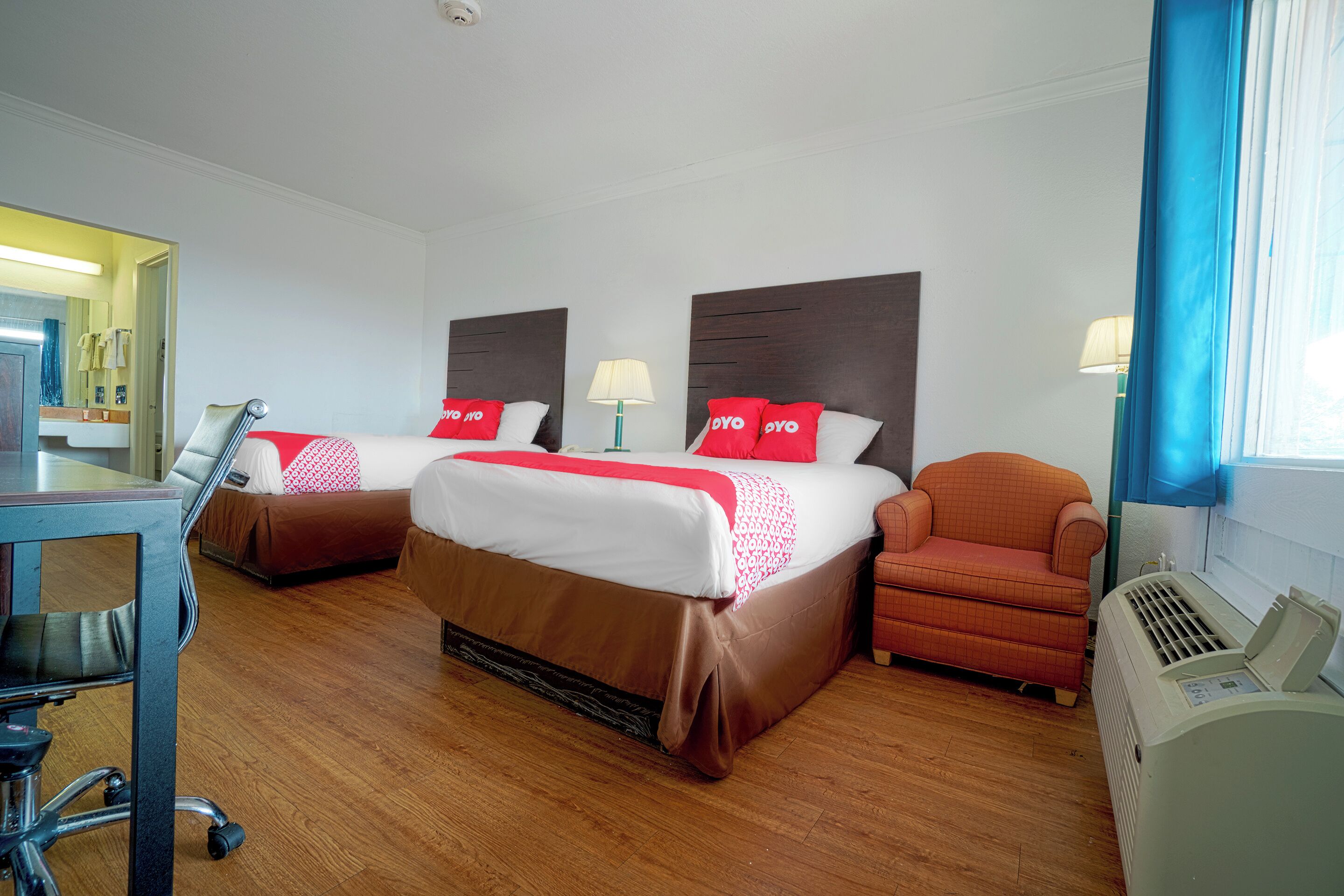 Une chambre d’hôtel avec deux lits, un bureau, une chaise et un radiateur.