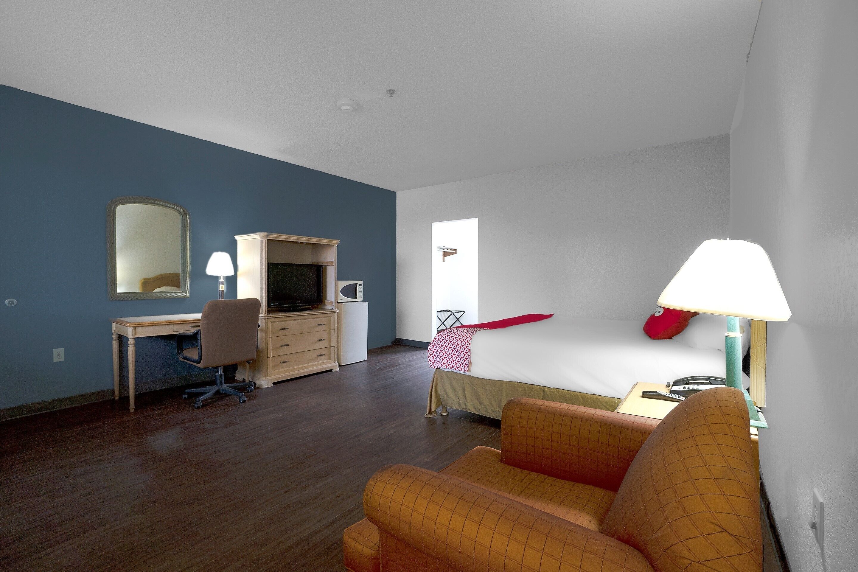 A room with a bed, a desk with a chair, a television, and a lamp.
