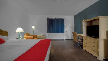 Quarto de hotel com cama, escrivaninha, televisão e uma cadeira.