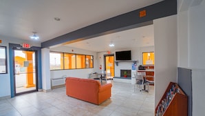 Un vestíbulo amplio con un sofá naranja grande, una chimenea y un televisor de pantalla plana montado en la pared.