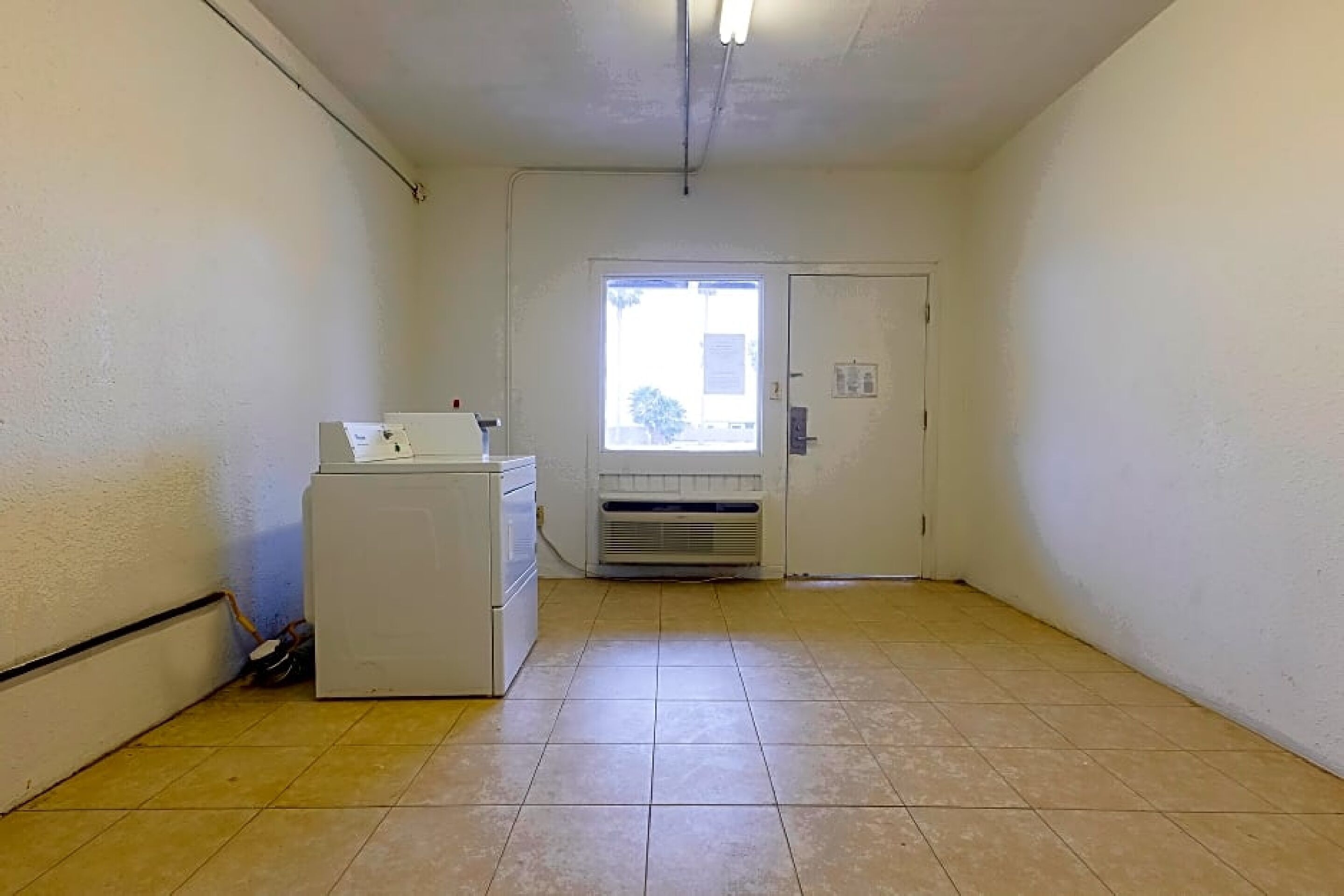 A small, clean room with a washing machine, a door with a window, and a tiled floor.