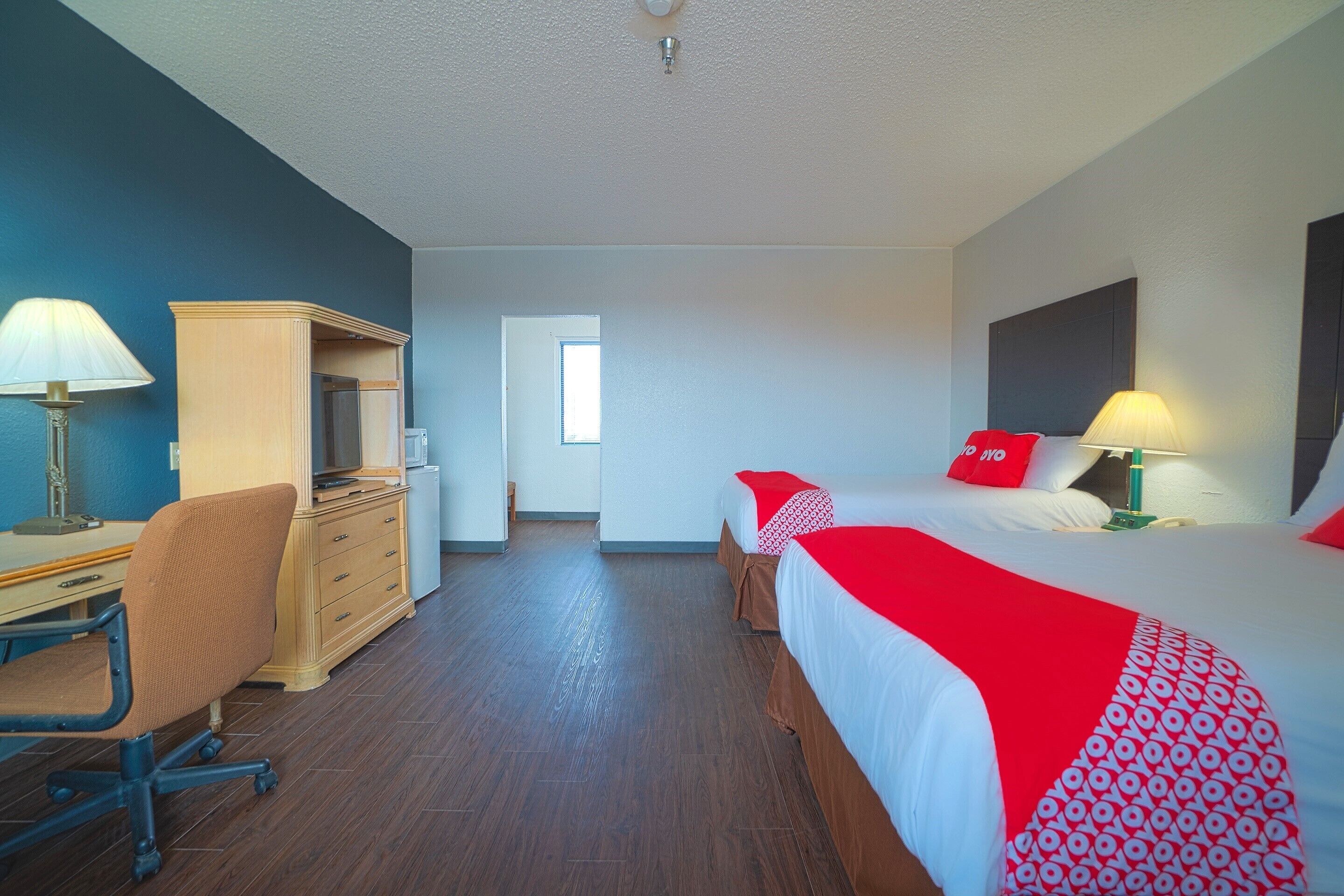 A hotel room with two beds, a desk, a chair, and a wardrobe.