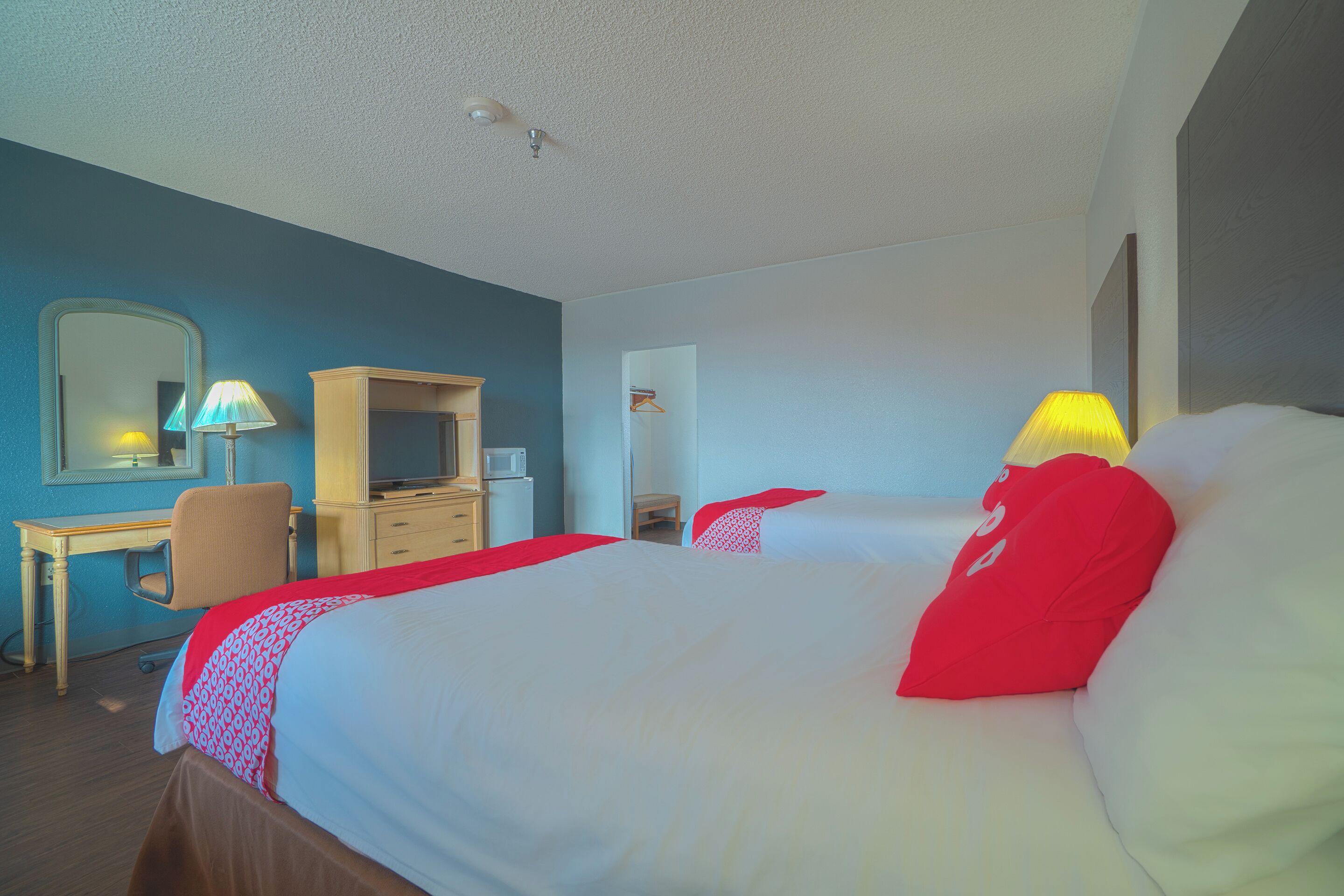 A hotel room with two beds, a desk, a chair, a dresser, and a mirror.