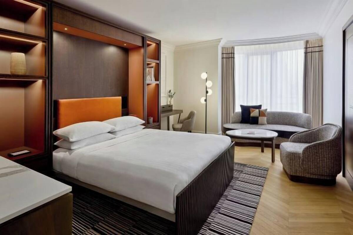 Una habitación de hotel con una cama grande, una zona de estar con sofá y sillones, una mesita y una lámpara de pie.