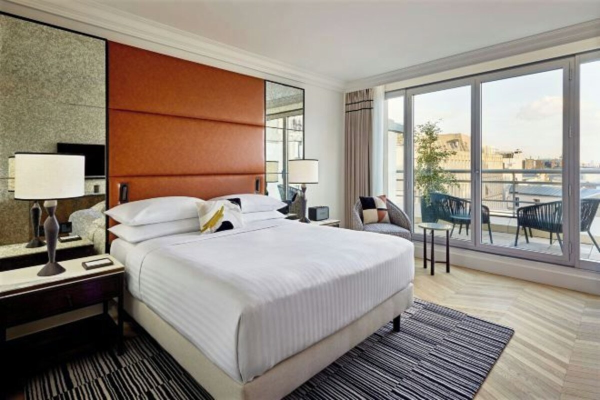 Een hotelkamer met een groot bed, uitzicht op de stad en een balkon met tuinmeubilair.